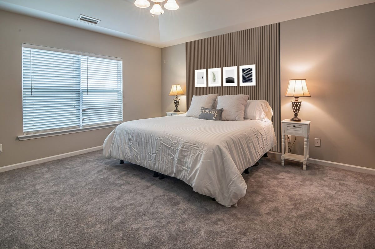 Four white frames on floor-to-ceiling smoked oak slats between two bedside lamps in a beige bedroom